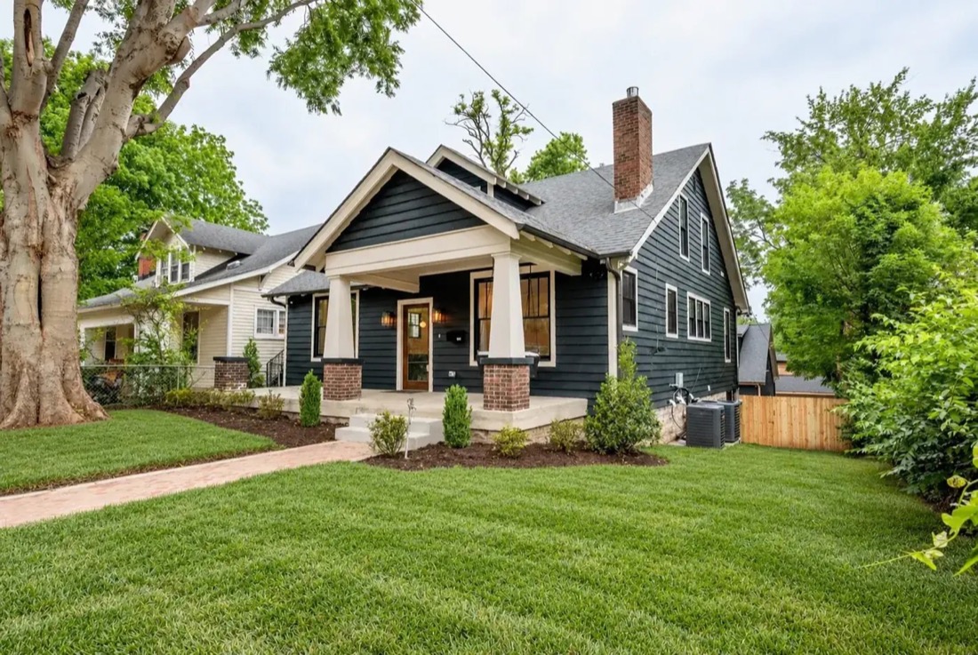 Dark green craftsman bungalow with white trim, brick porch columns and a deep front porch