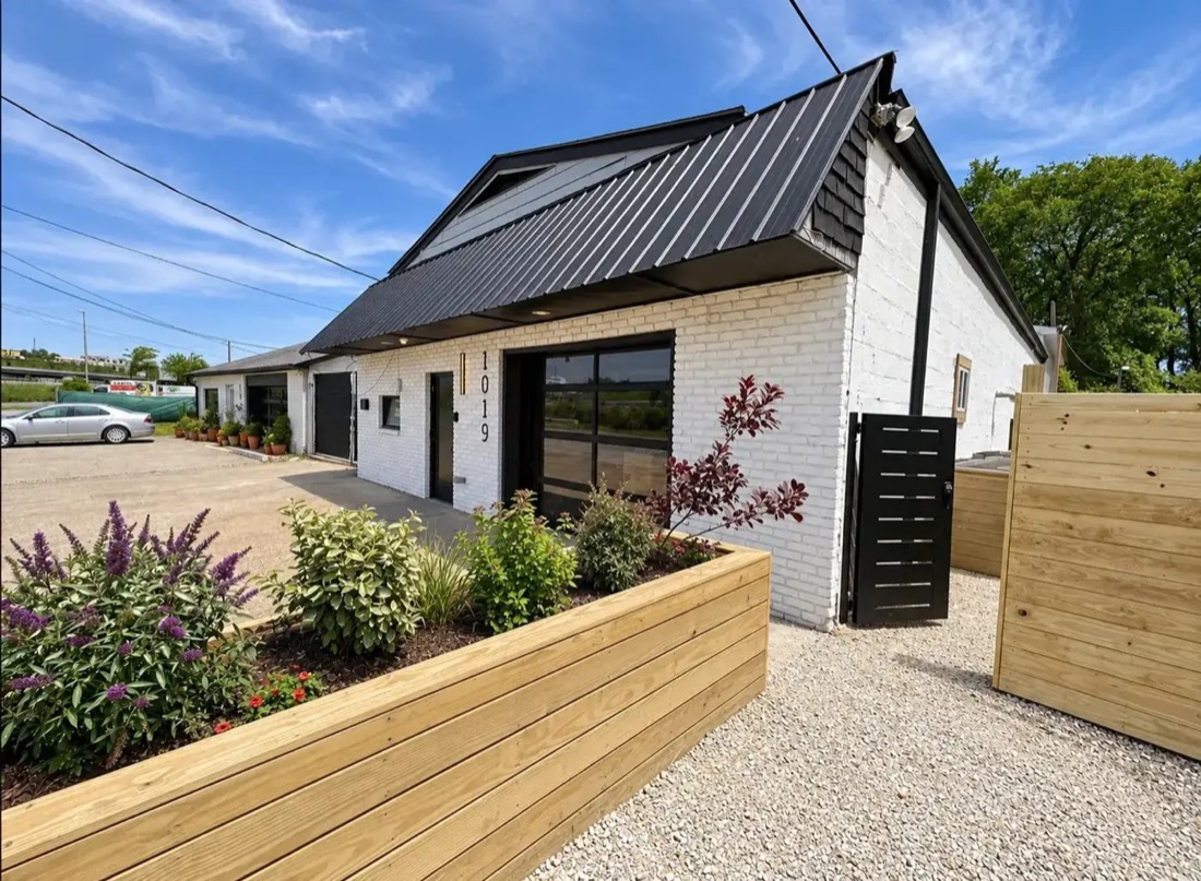 White painted brick building with a black metal roof and cedar planters